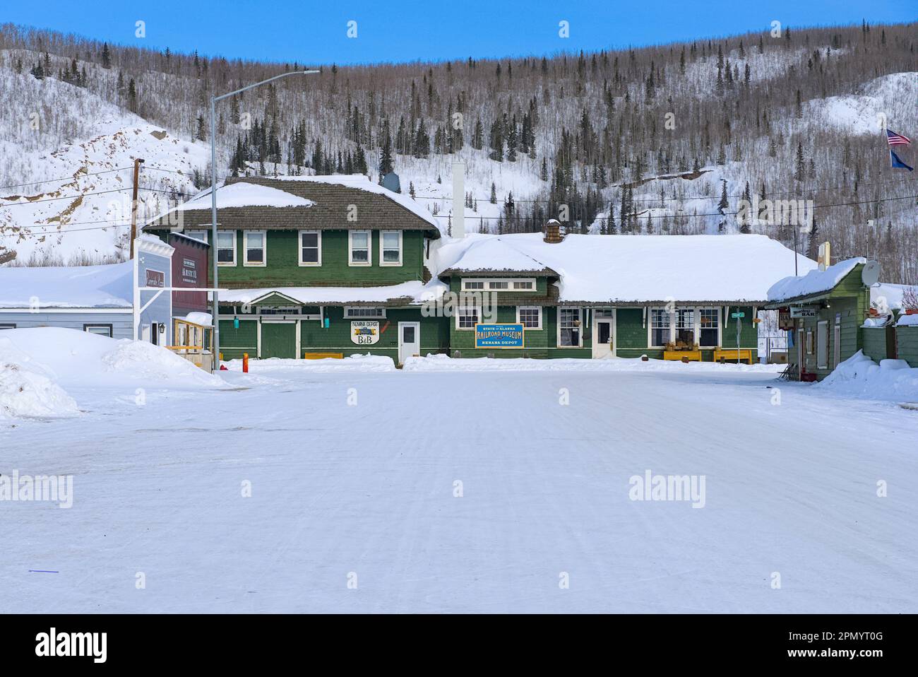 Ein kleines Gebäude vor einem Hügel am Ende der schneebedeckten Straße. Stockfoto