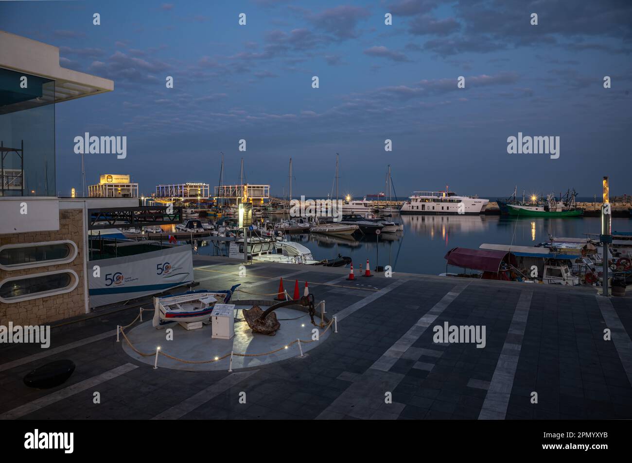 Limassol, Zypern - 23. März 2023 - Blick über den alten Hafen in der Abenddämmerung mit reflektierenden Booten, Gebäuden und bunten Nachtlichtern Stockfoto