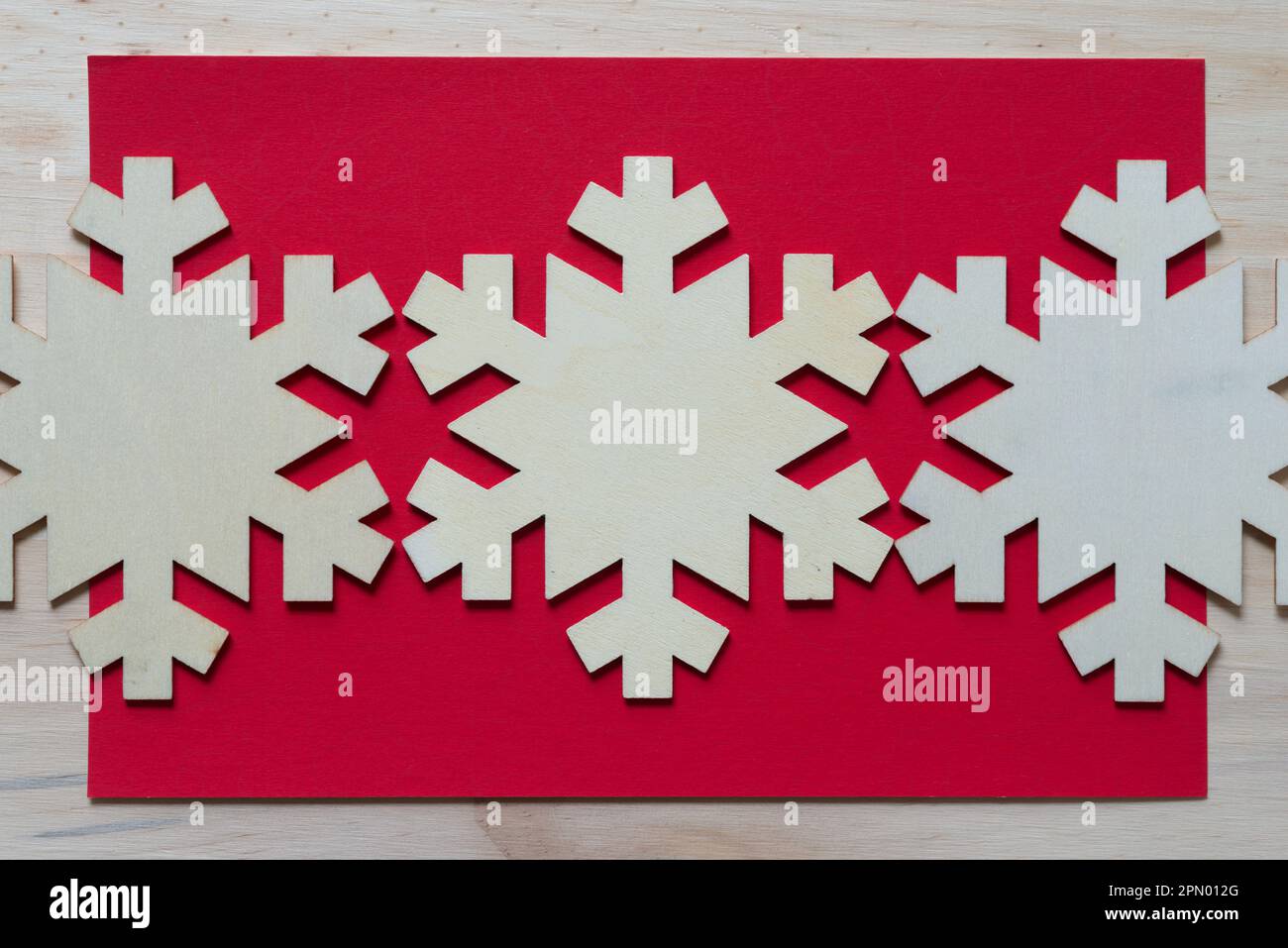 weihnachtsschmuck oder Schneeflockenschmuck auf rotem Papier und Holzplanke Stockfoto