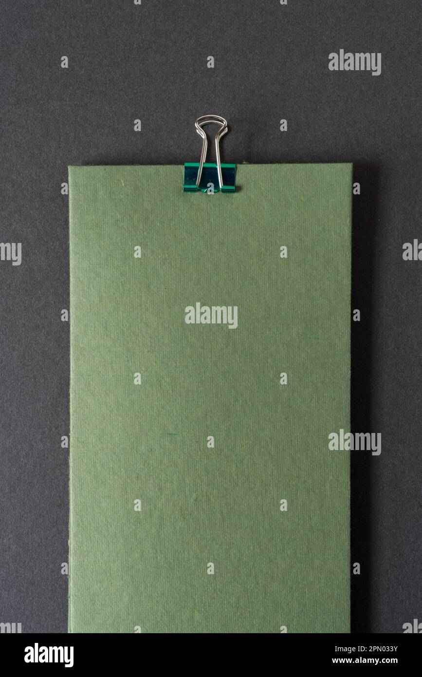 Raue grüne Papierkarte mit Metallklammer auf einem leeren Papierhintergrund Stockfoto