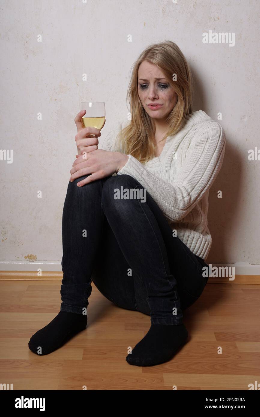 Traurige junge Frau sitzt auf dem Boden mit Glas Wein weinen Stockfoto