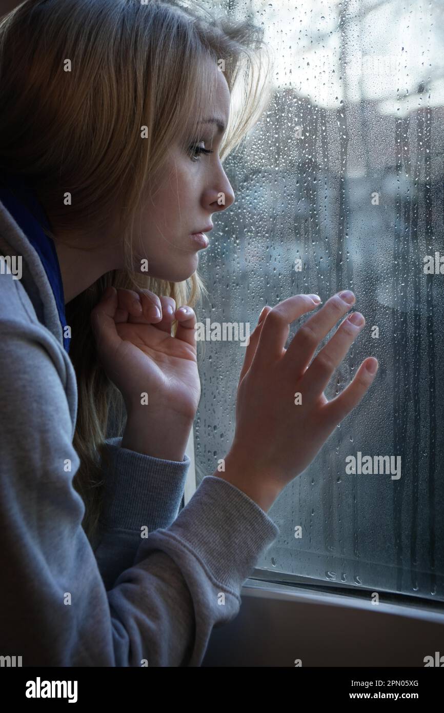 Traurige junge Frau auf der Suche durch das Fenster mit Regentropfen Stockfoto