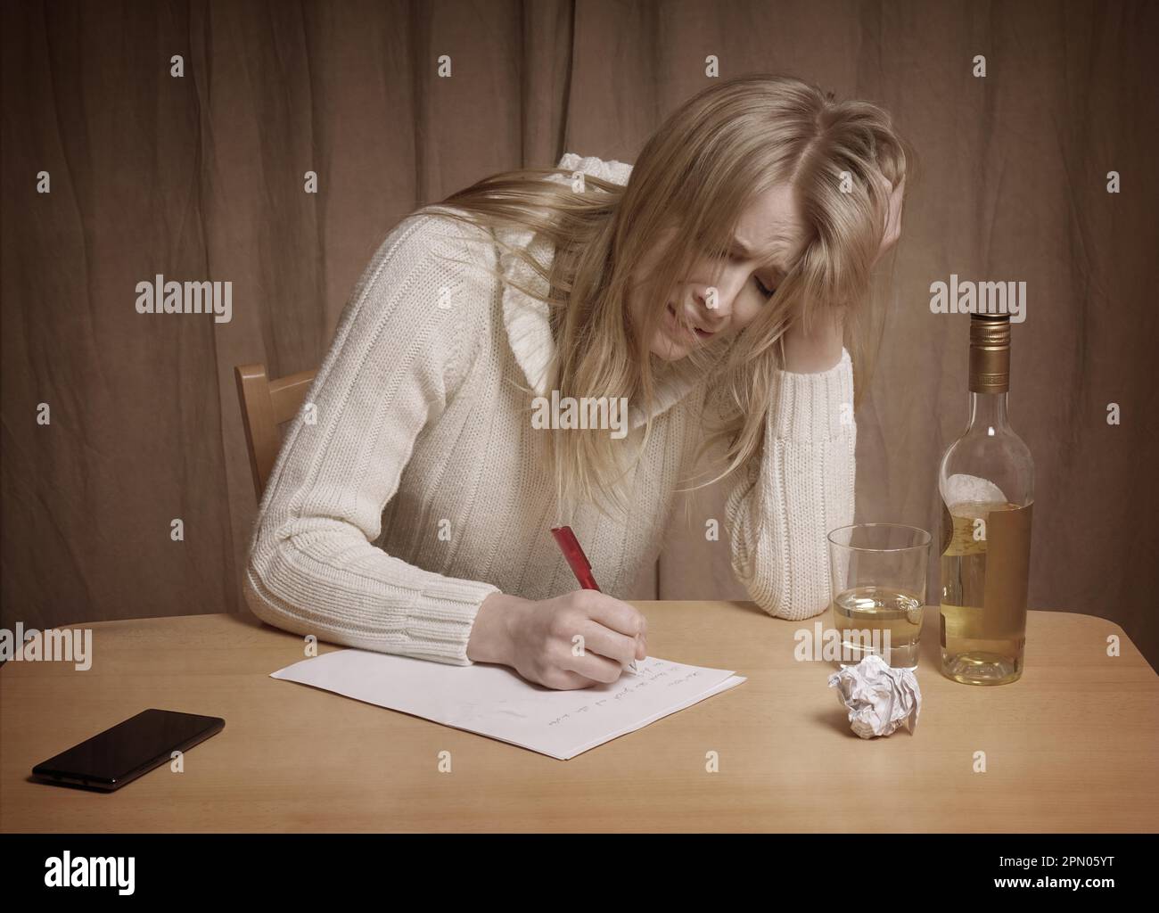 Verliebte junge Frau schreiben Brief mit einer Flasche Whiskey auf Tisch Stockfoto