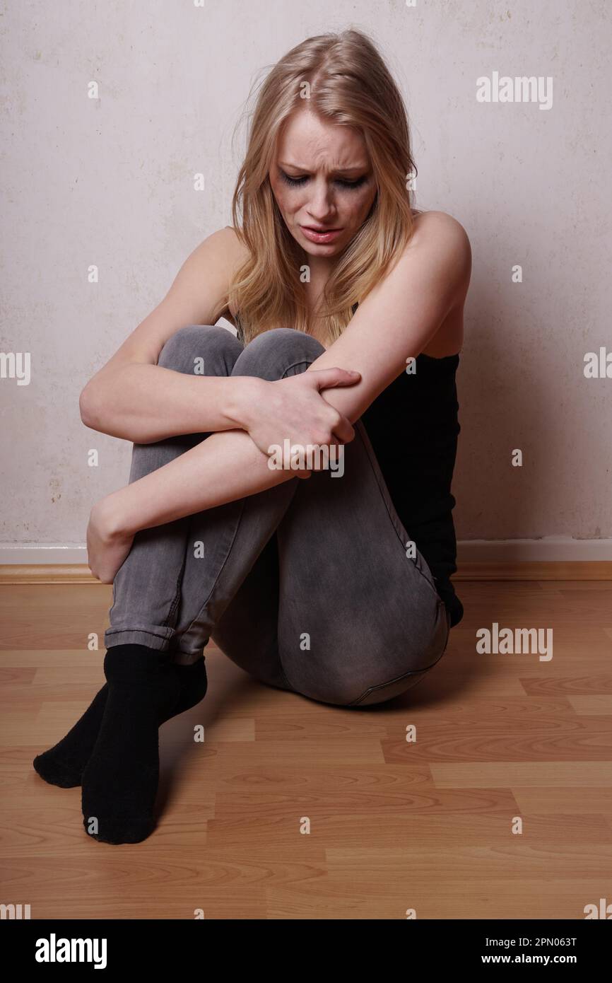 Traurige junge Frau mit verschmierter Wimperntusche und Tränen laufen über ihr Gesicht auf dem Boden sitzend Stockfoto