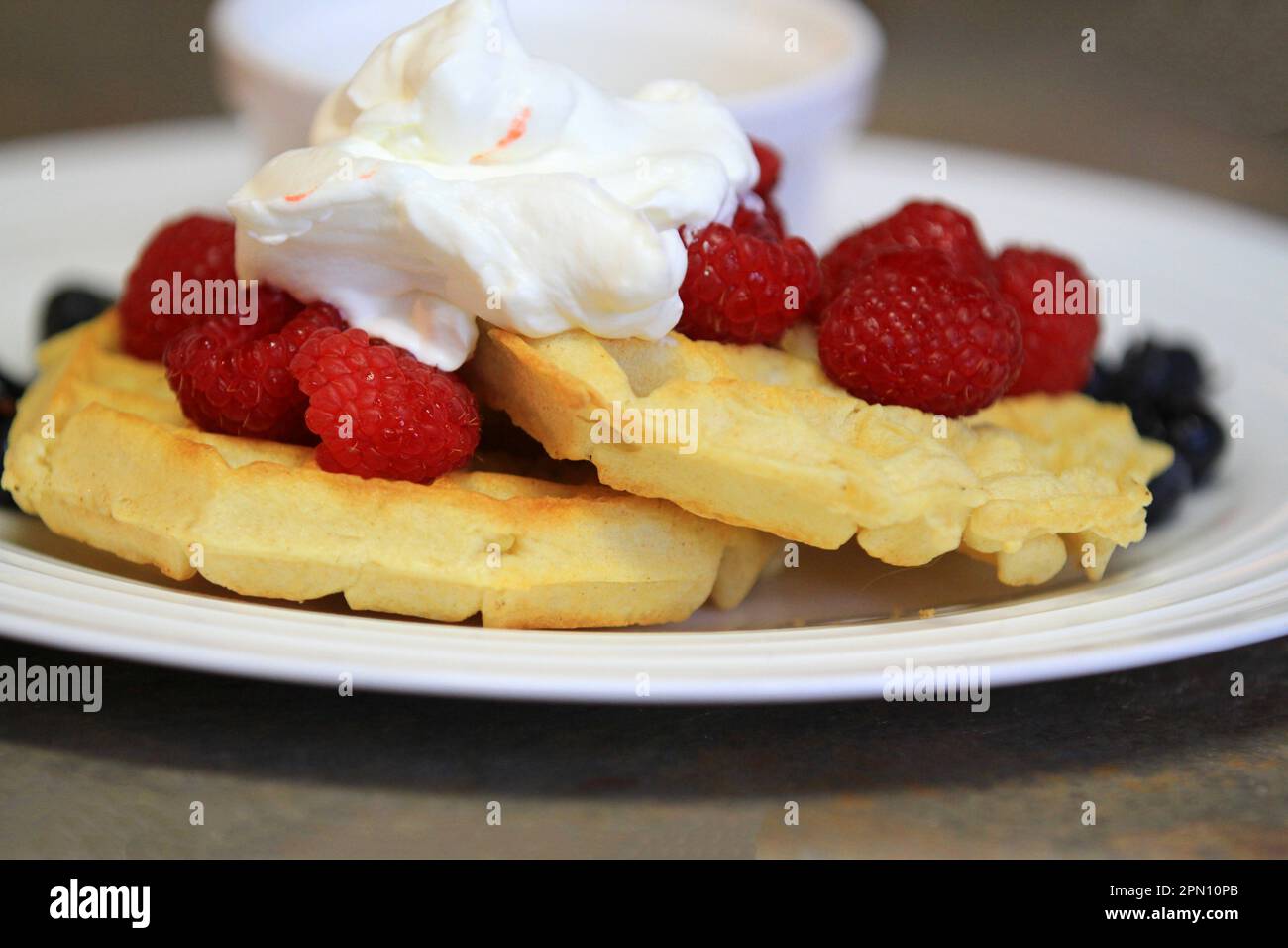 Frühstückswaffeln mit frischen Himbeeren, Heidelbeeren und Schlagsahne auf weißem Teller Stockfoto