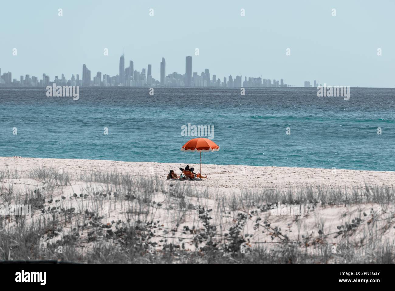 Strandszene mit begrenzter Farbpalette, mit einem Strandschirm am Kirra Beach und der Skyline von Surfers Paradise City am Horizont Stockfoto