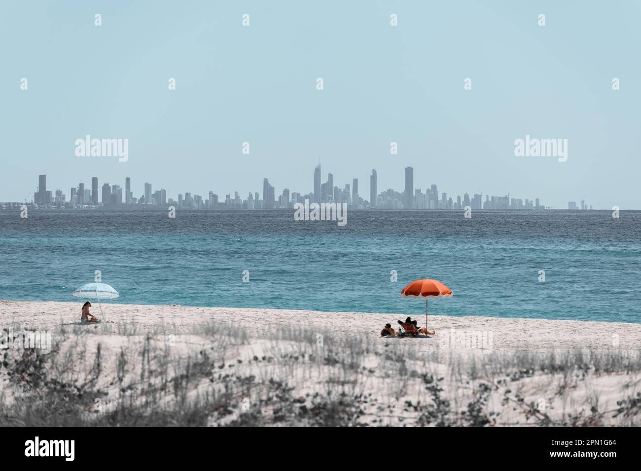 Strandszene mit begrenzter Farbpalette, mit Sonnenschirmen am Kirra Beach und der Skyline von Surfers Paradise City am Horizont Stockfoto