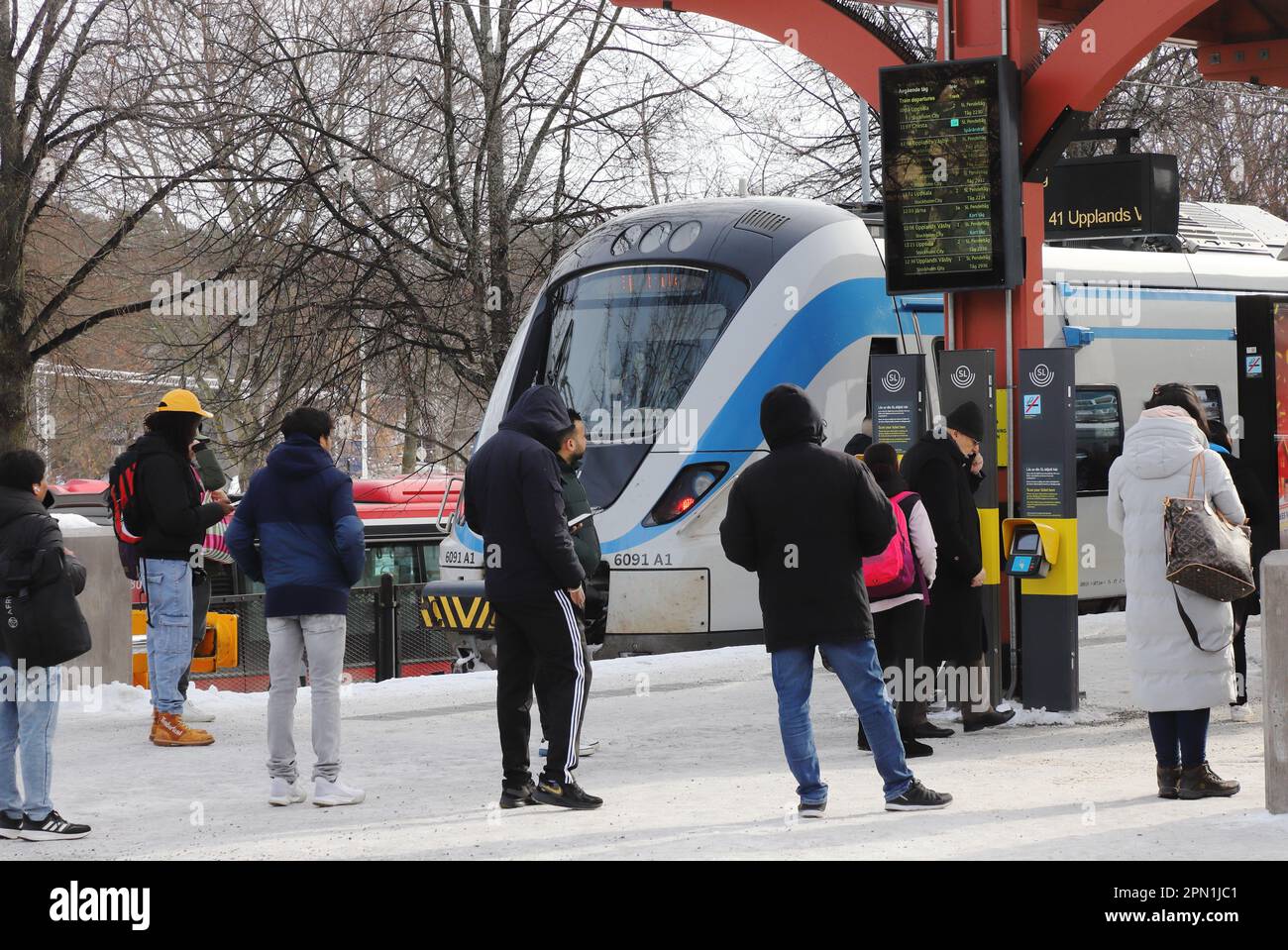 Sodertalje, Schweden - 11. März 2023: Menschen warten auf die Abfahrt am Bahnhof Sodertalje Centrum auf einer schneebedeckten Freiluftplattform Stockfoto