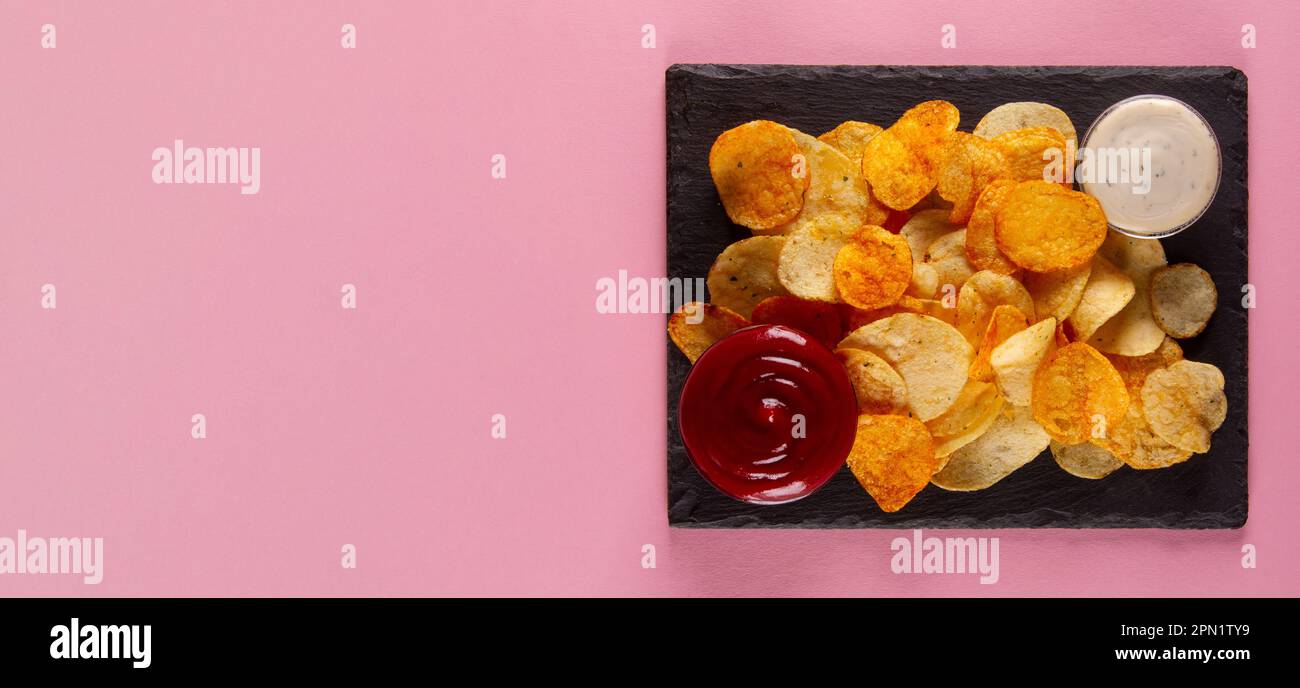 Perfekt gesalzene und knusprige Kartoffelchips mit cremeweißem und herzhaftem roten Dip auf pinkfarbenem Hintergrund Stockfoto