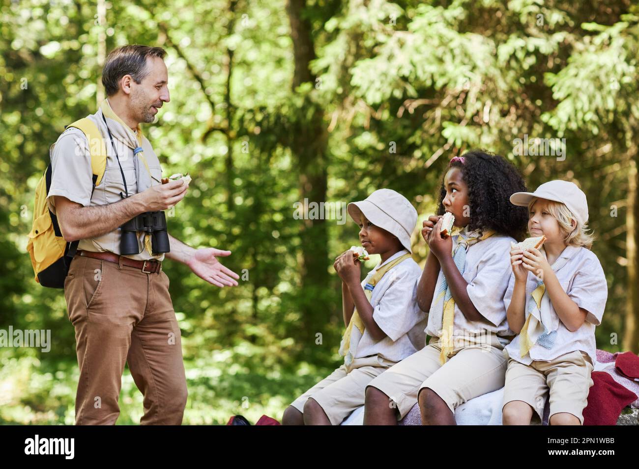 Seitliches Porträt eines erwachsenen Pfadfinders, der während der Wanderung mit der Gruppe o Kinder spricht Stockfoto