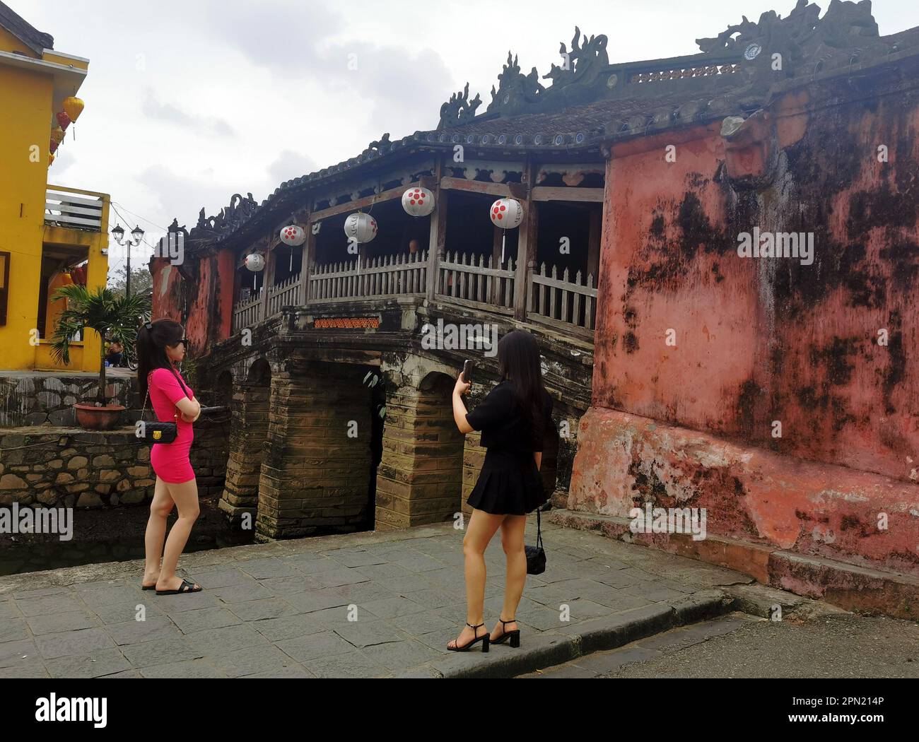 Hoi An, Vietnam. 02. März 2023. Zwei Frauen fotografieren sich vor der Chua Cau Bridge (auch japanische Brücke oder Lai Vien Kieu) in der Altstadt von Hoi an. Der Bau der Brücke vereinigte zwei historische Viertel der Stadt, die Chinesen auf der einen Seite und die Japaner auf der anderen. Die Grenze zwischen den Gebieten ist der 18 Meter lange bedeckte Chua Cau, der einen Nebenfluss des Thu Bon durchquert. Kredit: Alexandra Schuler/dpa/Alamy Live News Stockfoto