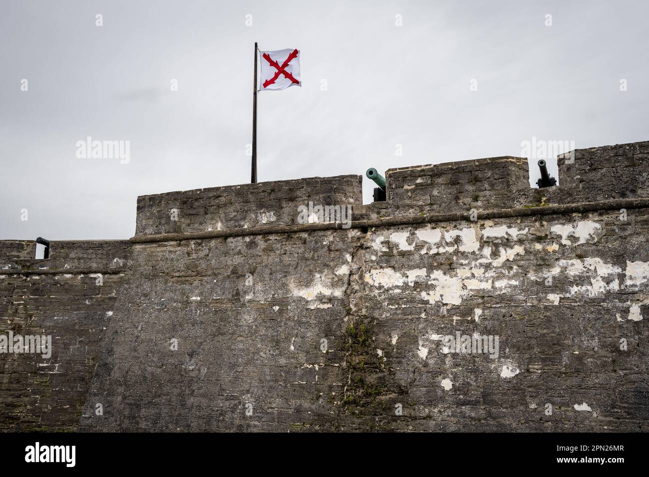 Spanische Kolonialflagge, die über den Steinmauern und Kanonen von Castillo de San Marcos, einer historischen Küstenfestung in St. Augustine, Florida, weht. Stockfoto