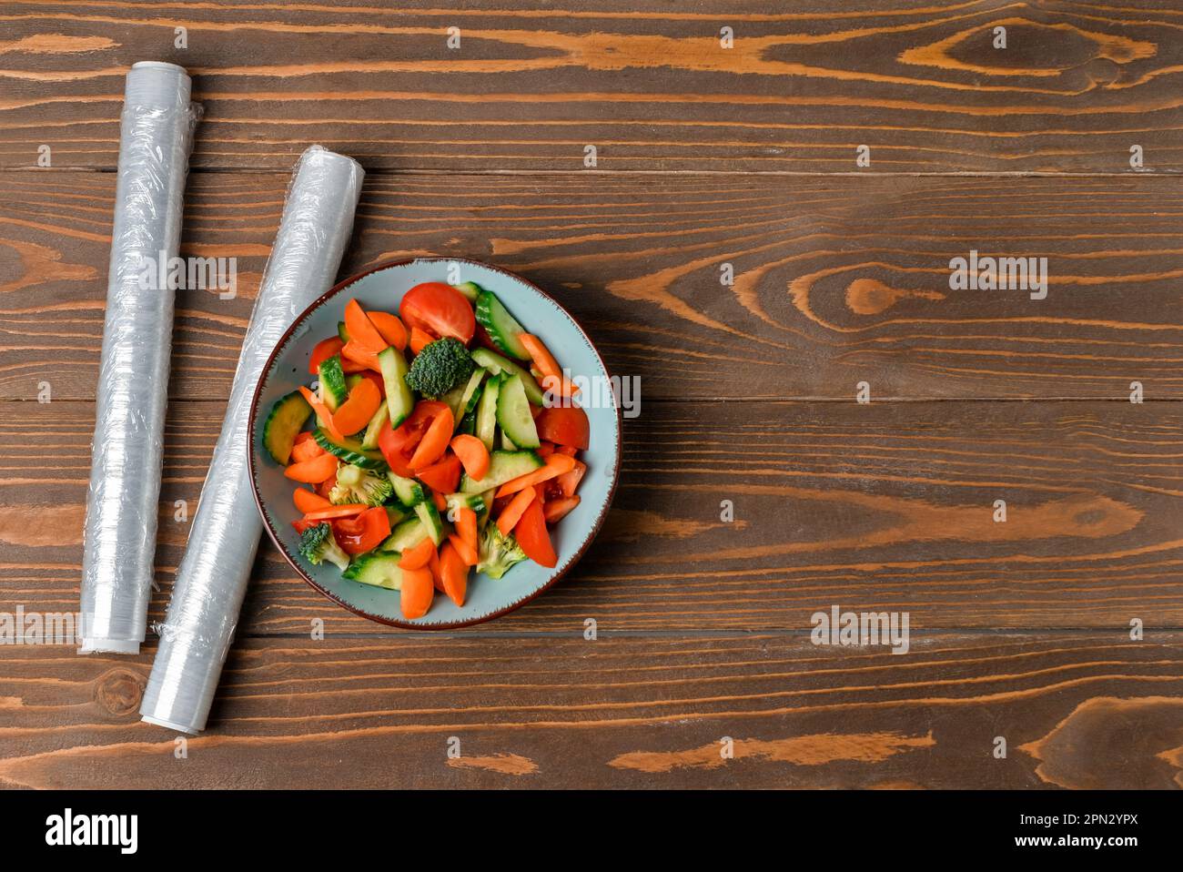 Schüssel mit Salat und Rollen Stretchfolie auf Holzhintergrund Stockfoto