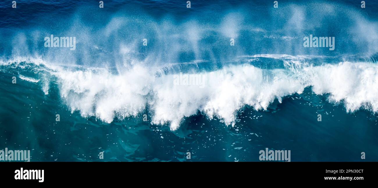 In diesem atemberaubenden Luftfoto wird eine gewaltige, stürzende Welle des Ozeans festgehalten, wobei die massive Welle in ein weißes Sprühnebel gegen das Wasser zerbricht. Stockfoto