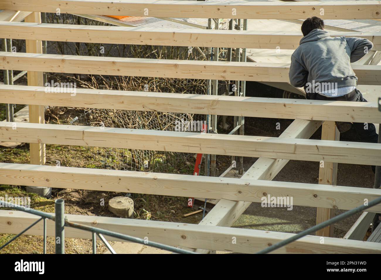 Bauholz, das auf dem Dachsparren arbeitet, einen Carport baut. Rückansicht des jungen Zimmermanns. Stockfoto