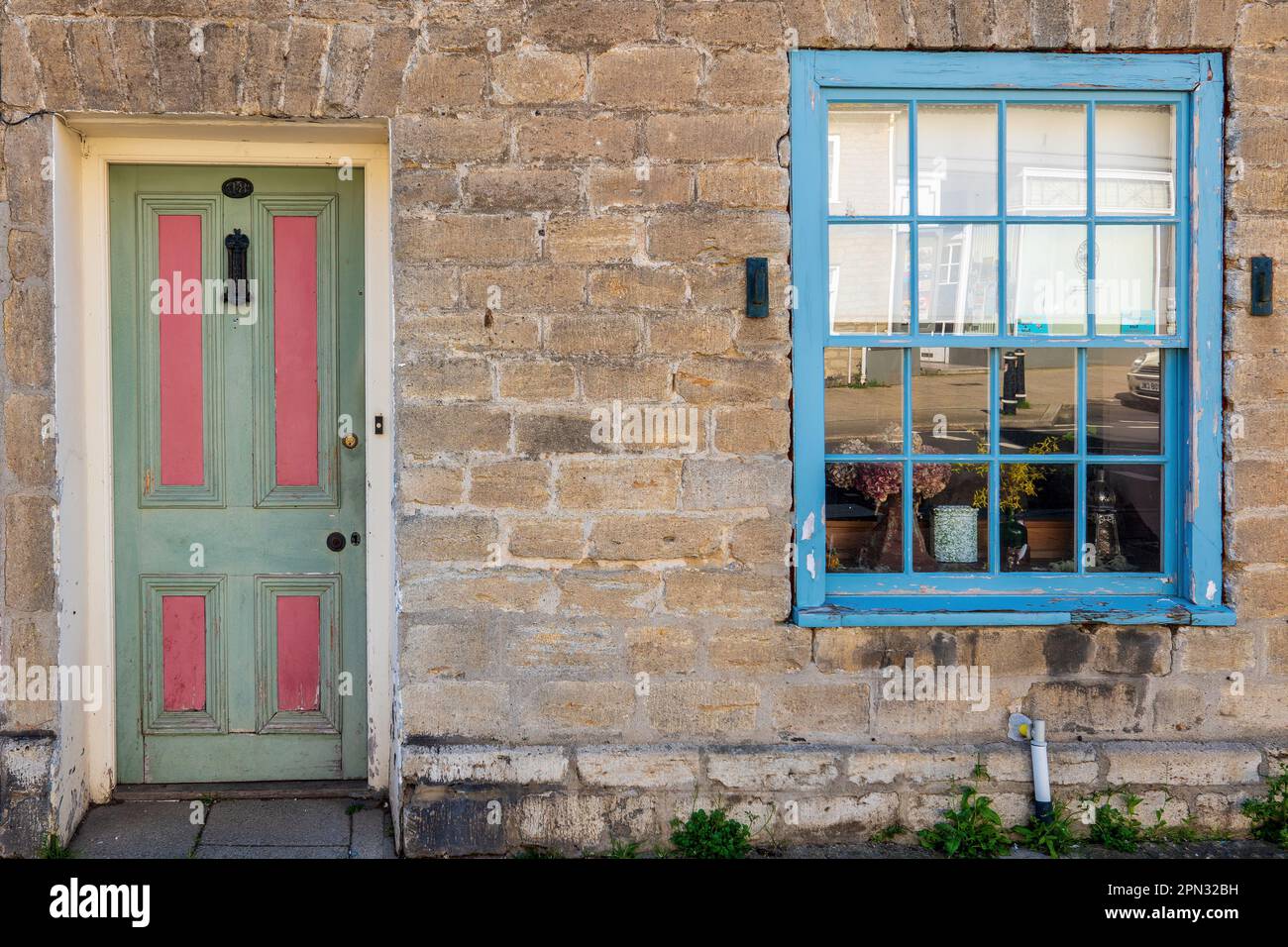 Pastellrosa und grün Eingangstür und Schiebefenster uof ein traditionelles georgianisches Cottage in Bridport, Dorset. Konzept traditionelle Hüttenfront. Stockfoto