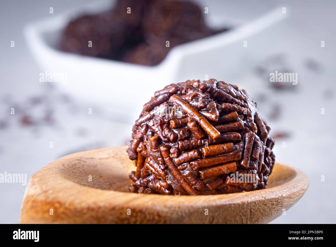 Die „Brigadier“-Süßigkeiten werden in einem Holzlöffel mit mehreren „brigadeiro“-Süßigkeiten auf einer weißen Schüssel hergestellt, auf dem Schokoladenstreusel liegen. Video schließen Stockfoto