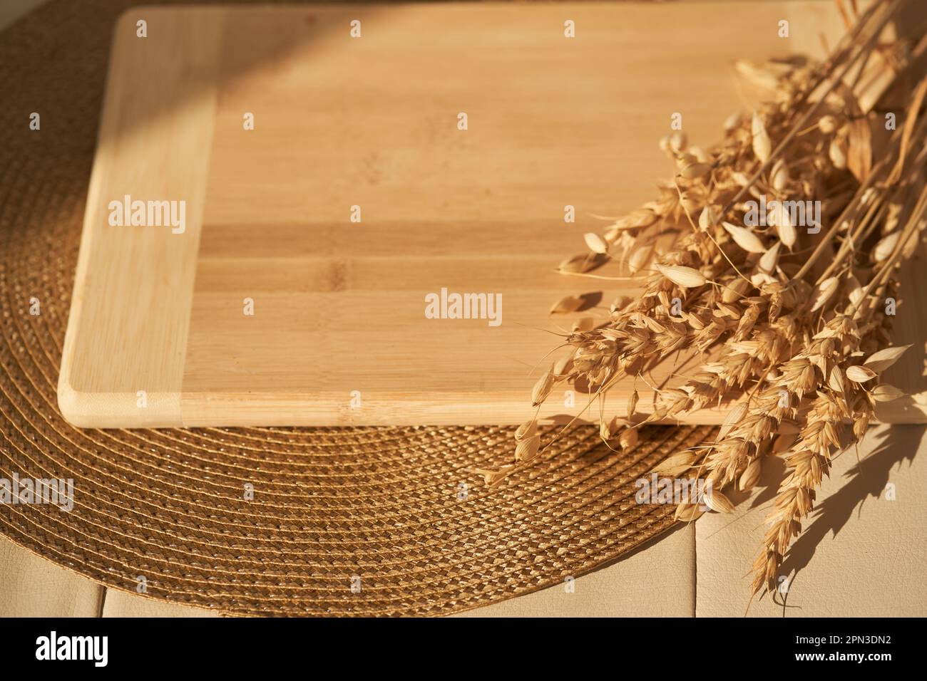 Ein leeres Schneidebrett liegt auf einer Serviette und in der Sonne, neben Weizen- und Roggenkörnern, einem Layout für Ihr Produkt, einem Podium für Ihr Brot oder Backen mit Kopierraum. Hochwertiges Foto Stockfoto