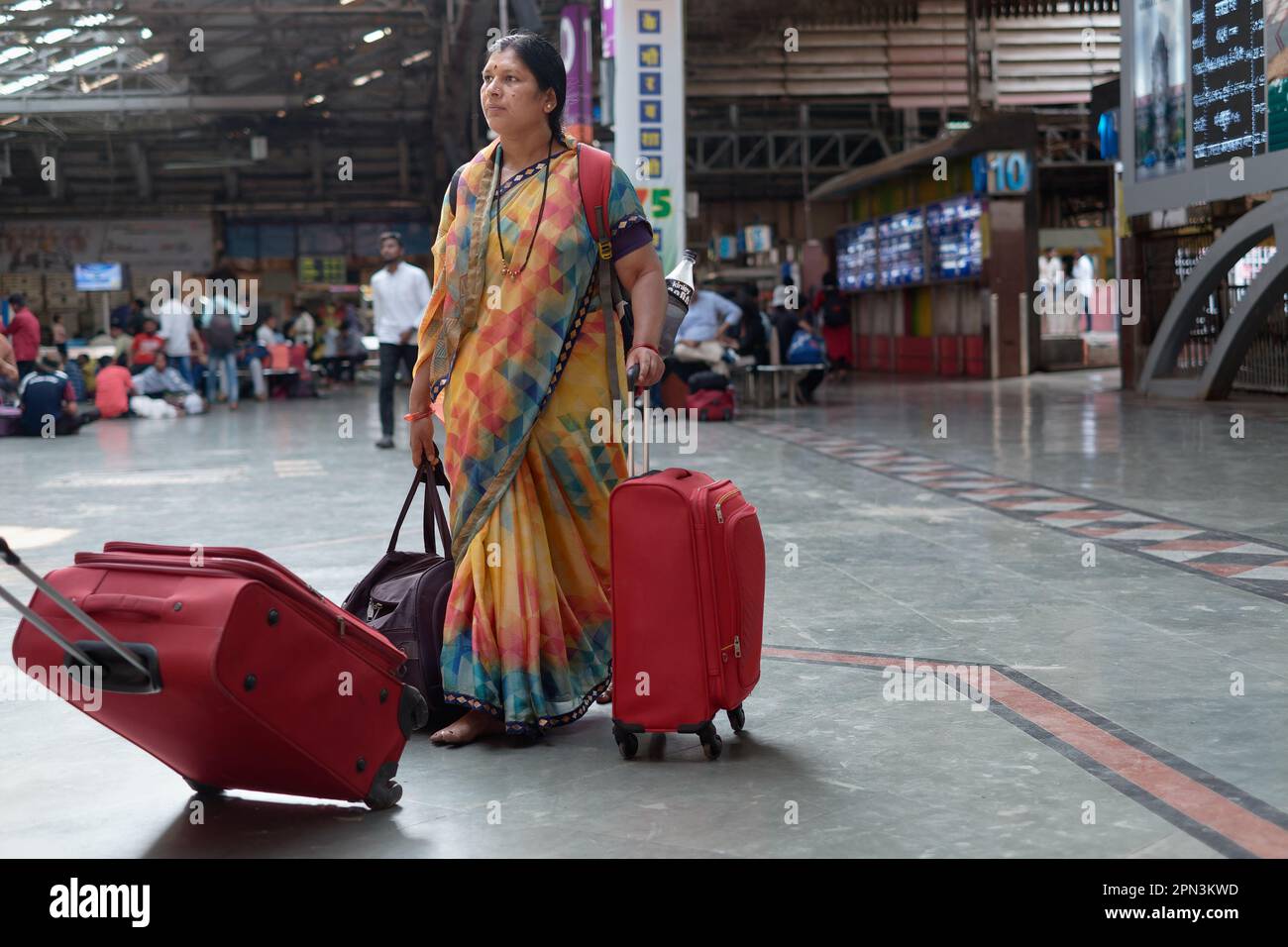 Eine in einem farbenfrohen Sari verkleidete Indianerin, die ihr Gepäck durch (Bahnhof) Chhatrapati Shivaji Maharaj Terminus in Mumbai, Indien zieht Stockfoto