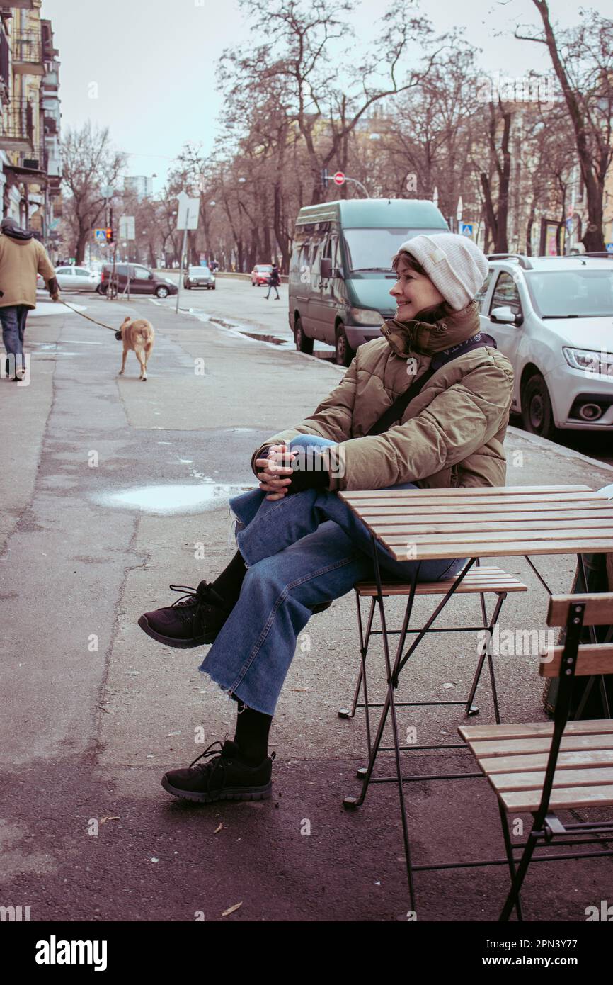 Lächelndes Mädchen, das im Straßencafé sitzt. Frühlingsmode. Mädchen mit Hut sitzt auf der Straße mit Hund. Großstadtleben. Urbaner Lifestyle. Stockfoto