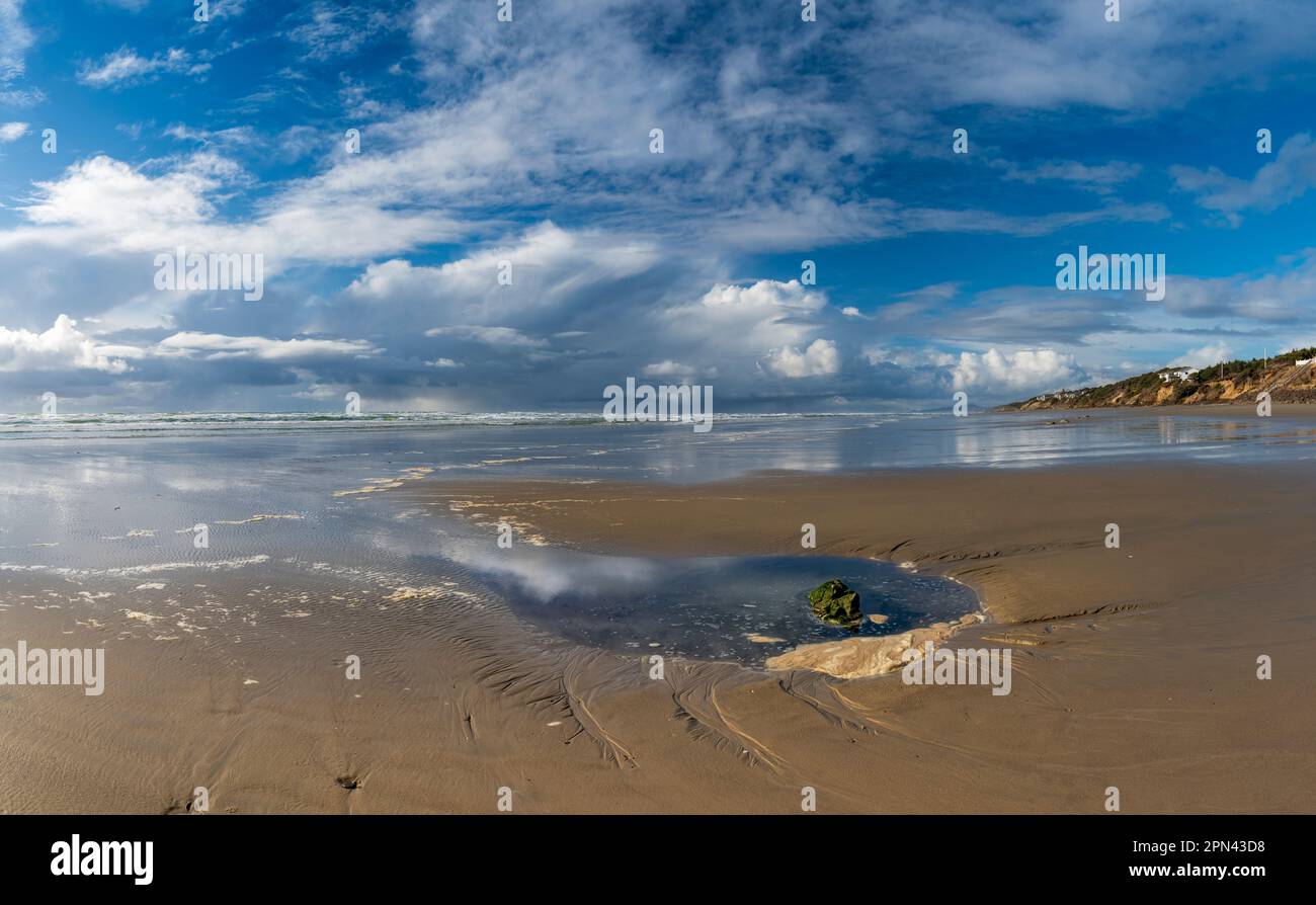Das Wasser des Gezeitenpools spiegelt den lebendigen Himmel wider und umgibt einen einsamen Felsen, der von Algen bedeckt ist, an einem Strand an der Pazifikküste Stockfoto