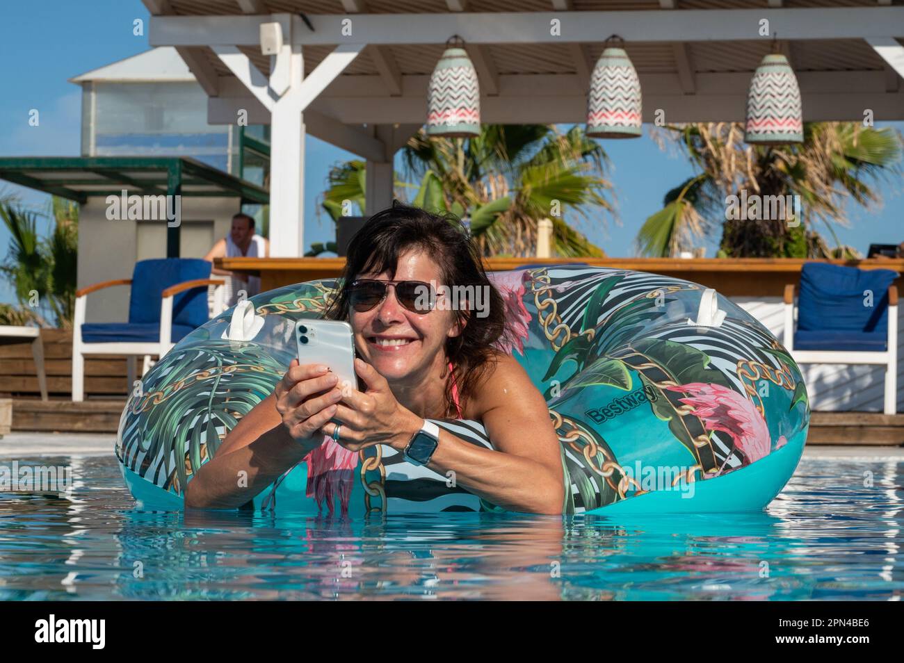 Aktive 60-jährige Frau, die ein Smartphone benutzt und im Urlaub im Pool lebt Stockfoto