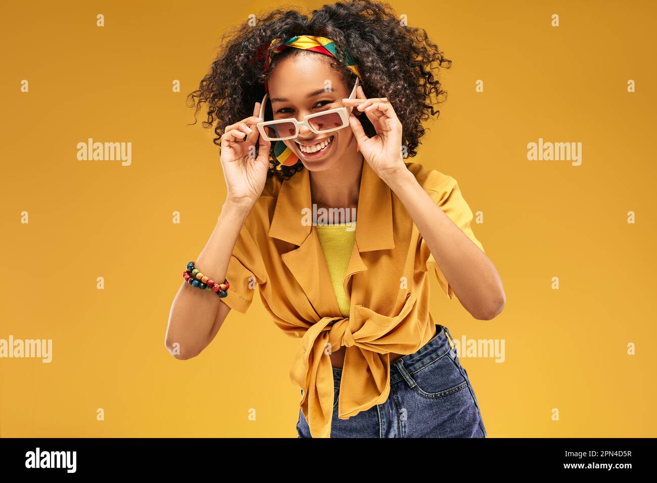 Fröhliches Mädchen trägt trendige weiße Sonnenbrille in farbenfroher trendiger Kleidung und genießt den Sommer-Style, Studioporträt auf Gelb Stockfoto