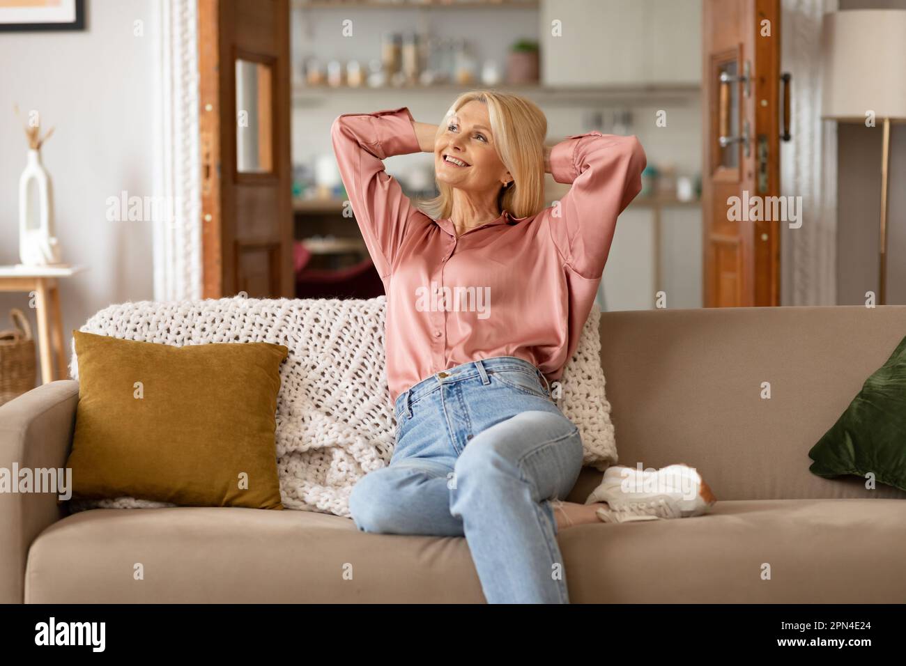 Fröhliche Blonde, Reife Frau, Die Zu Hause Auf Der Couch Sitzt Und Sich Entspannt Stockfoto