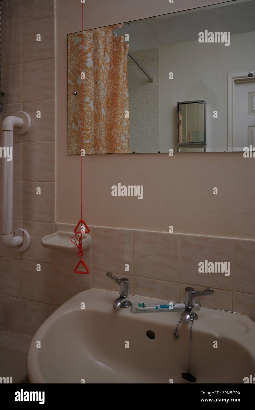 Altes Bad in Gelb mit orangefarbener Notzugschnur, Spiegel, Badezimmerschrank, Duschvorhang, Handlauf, Fliesen, Spüle, Zahnbürste und separates chr Stockfoto
