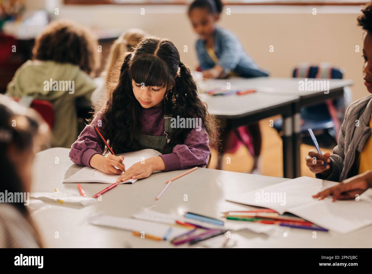 Kreatives junges Mädchen, das mit einem Bleistift in einer Klasse zeichnet. Eine Grundschülerin übt ihre Kunstfertigkeiten, während sie mit ihrem Schwanz in einem Klassenzimmer sitzt Stockfoto
