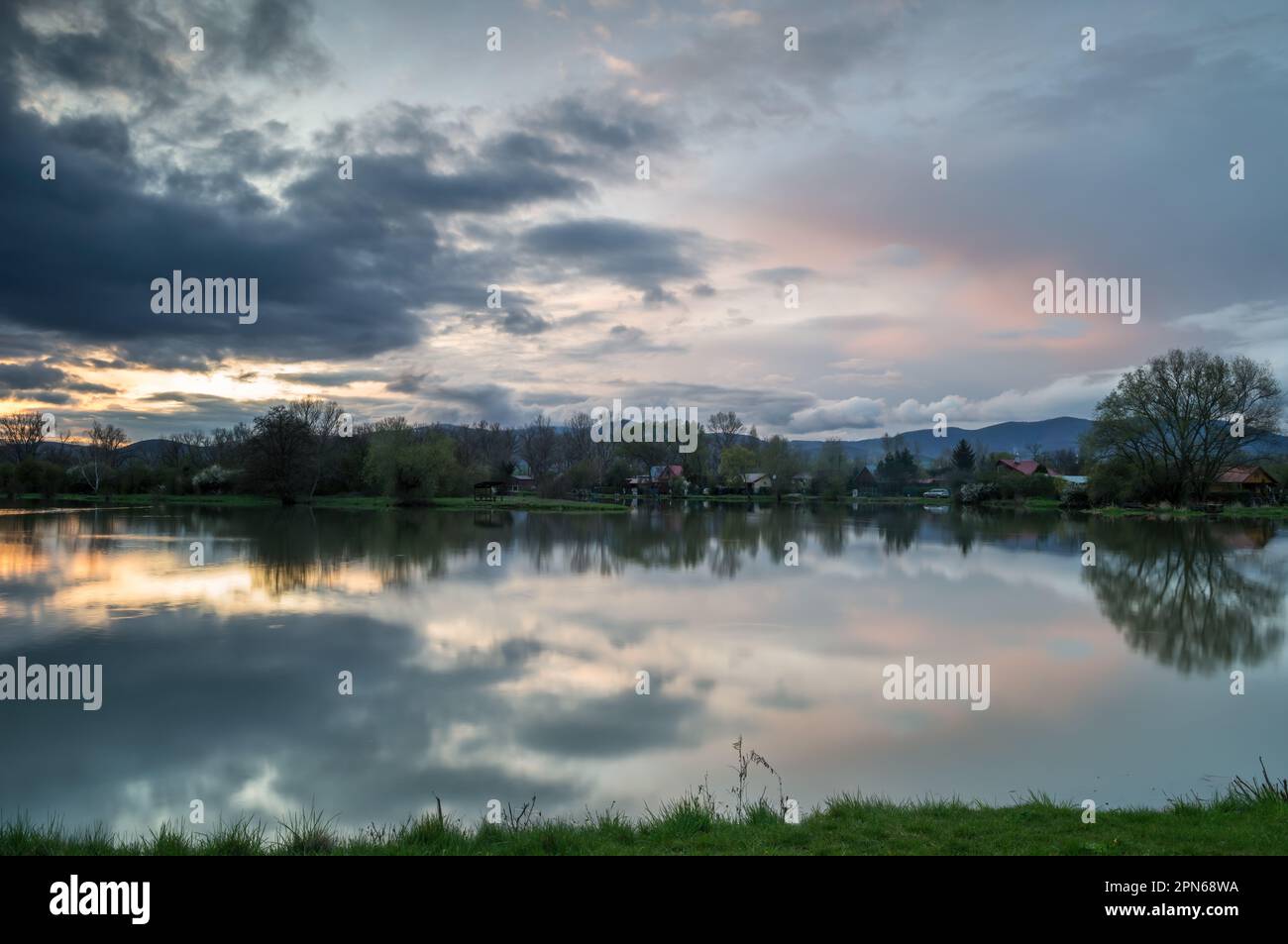 Abendliche Frühlingslandschaft. Teich mit Sturmwolken nach Regen bei Sonnenuntergang, mit einer ruhigen Wasseroberfläche und Wolkenreflexion. Bodovka, Slowakei. Stockfoto