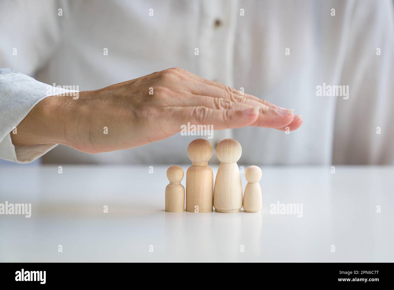 Die Hand bedeckt die hölzerne Puppenfamilie mit Vater, Mutter, Tochter und Sohn. Familienbetreuungs- und Schutzkonzept. Stockfoto