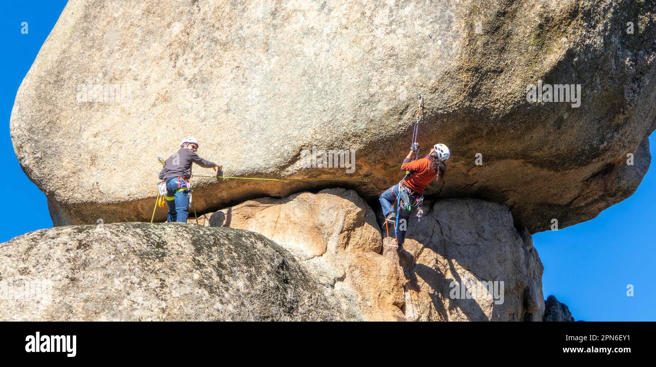 Zwei junge Erwachsene arbeiten zusammen, um eine Granitmauer zu erklimmen. Felsklettern. Extremsportkonzept Stockfoto