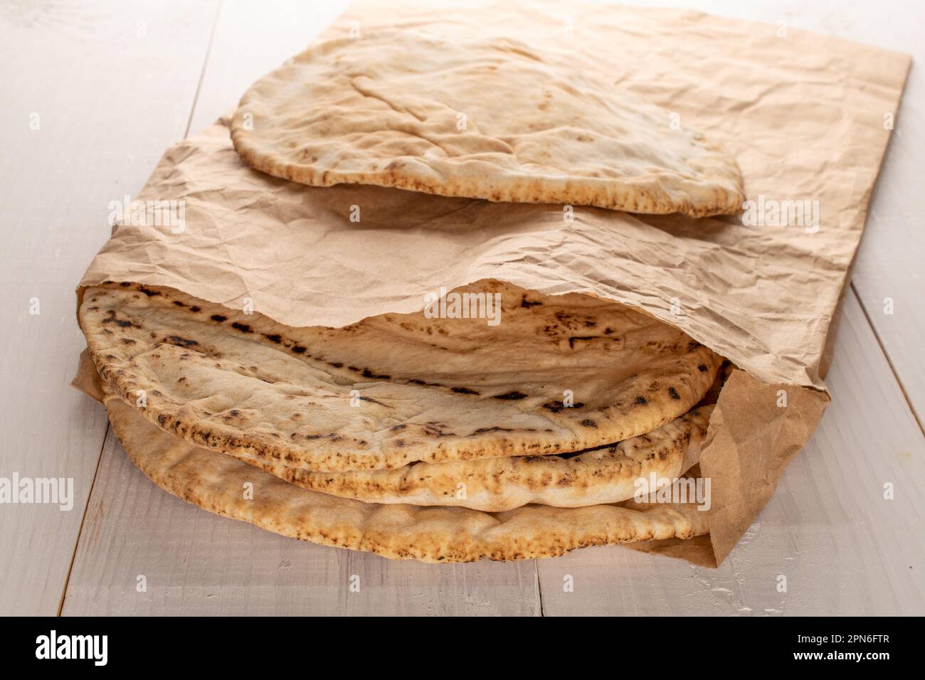 Mehrere frisch gebackene Pita-Brote in einer Papiertüte, Nahaufnahme, auf einem Holztisch. Stockfoto