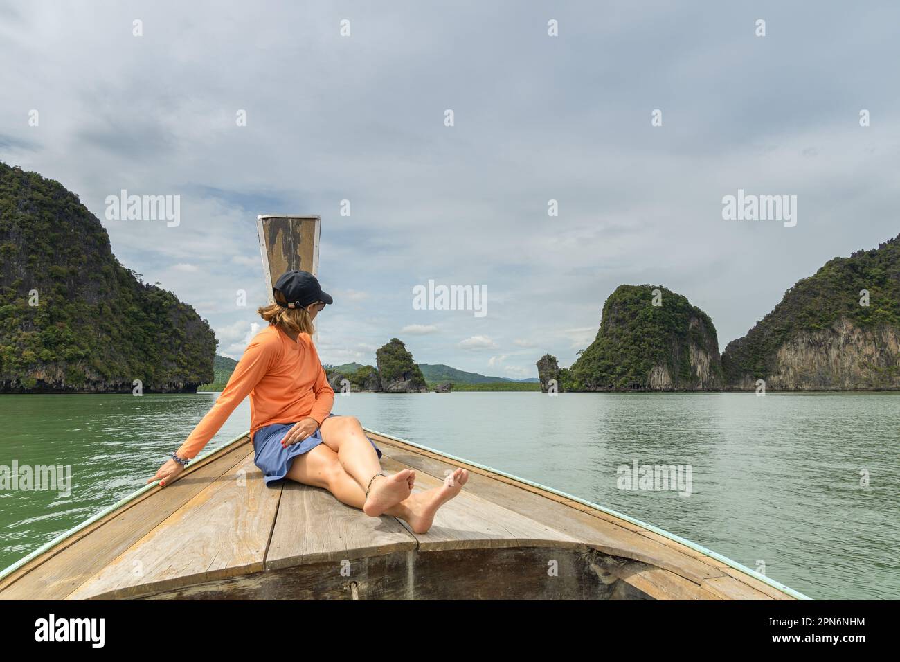 Reisende Frau, die in einem typischen thailändischen Boot sitzt und die Berglandschaft bewundert Stockfoto