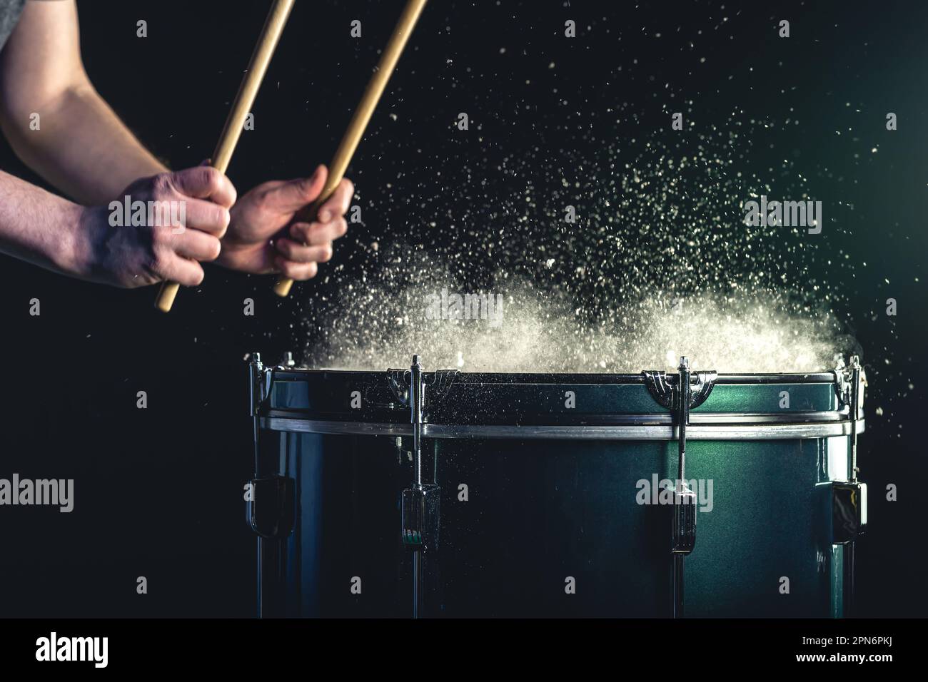 Ein Mann spielt ein musikalisches Schlaginstrument mit Stöcken auf dunklem Hintergrund. Stockfoto