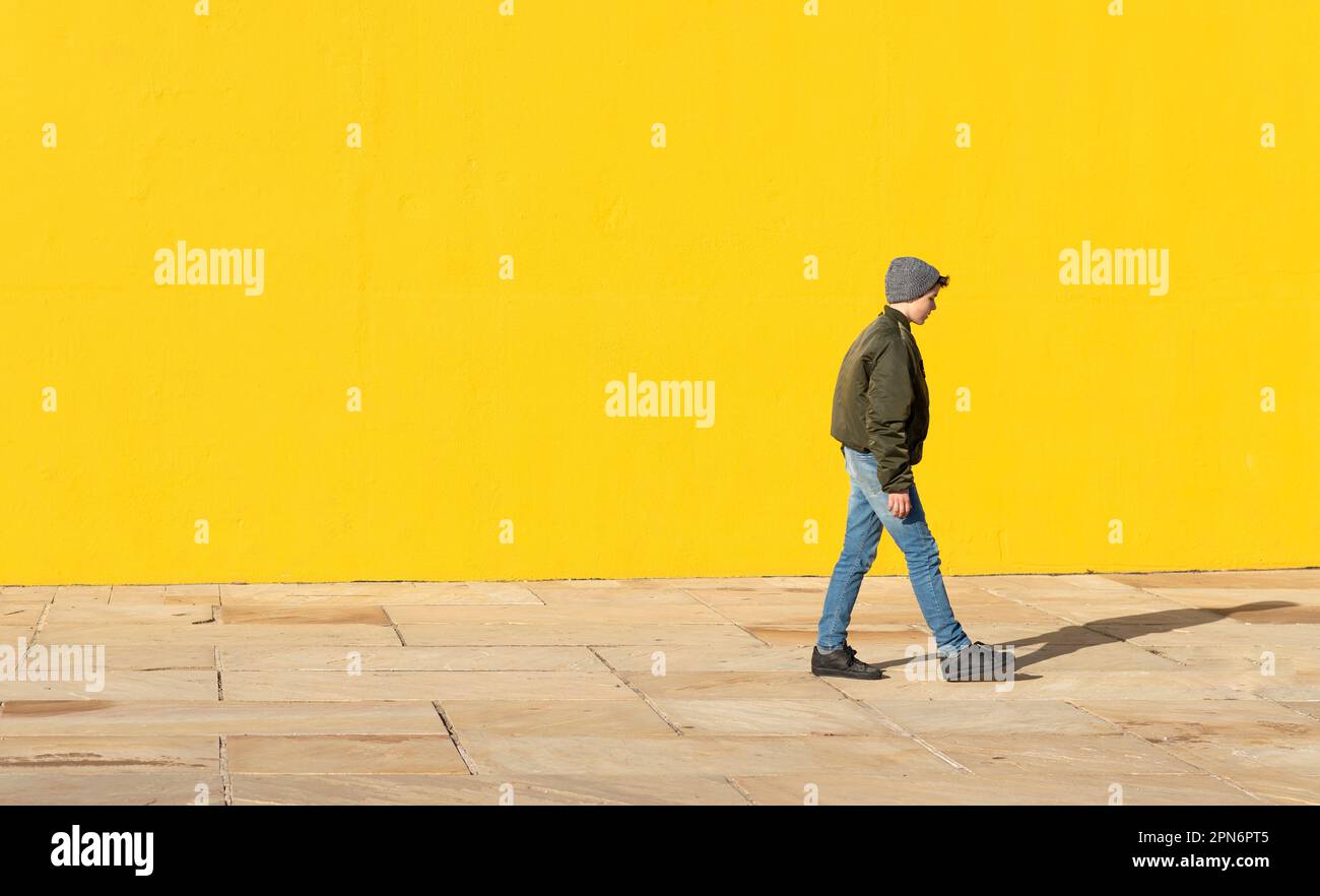 Seitenansicht eines jungen Teenagers, das zu einer gelben Mauer geht Stockfoto