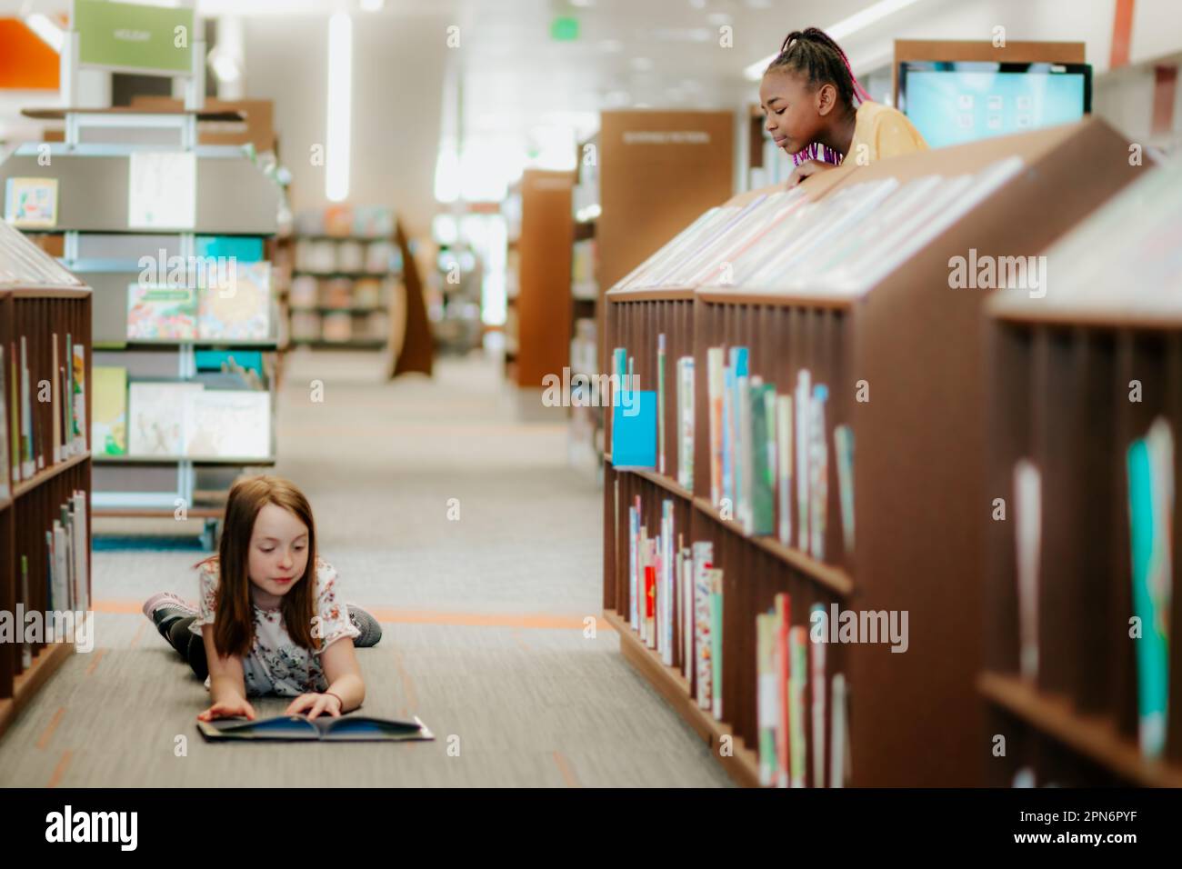 Mädchen, die einem Freund beim Lesen in der Bibliothek zusieht Stockfoto