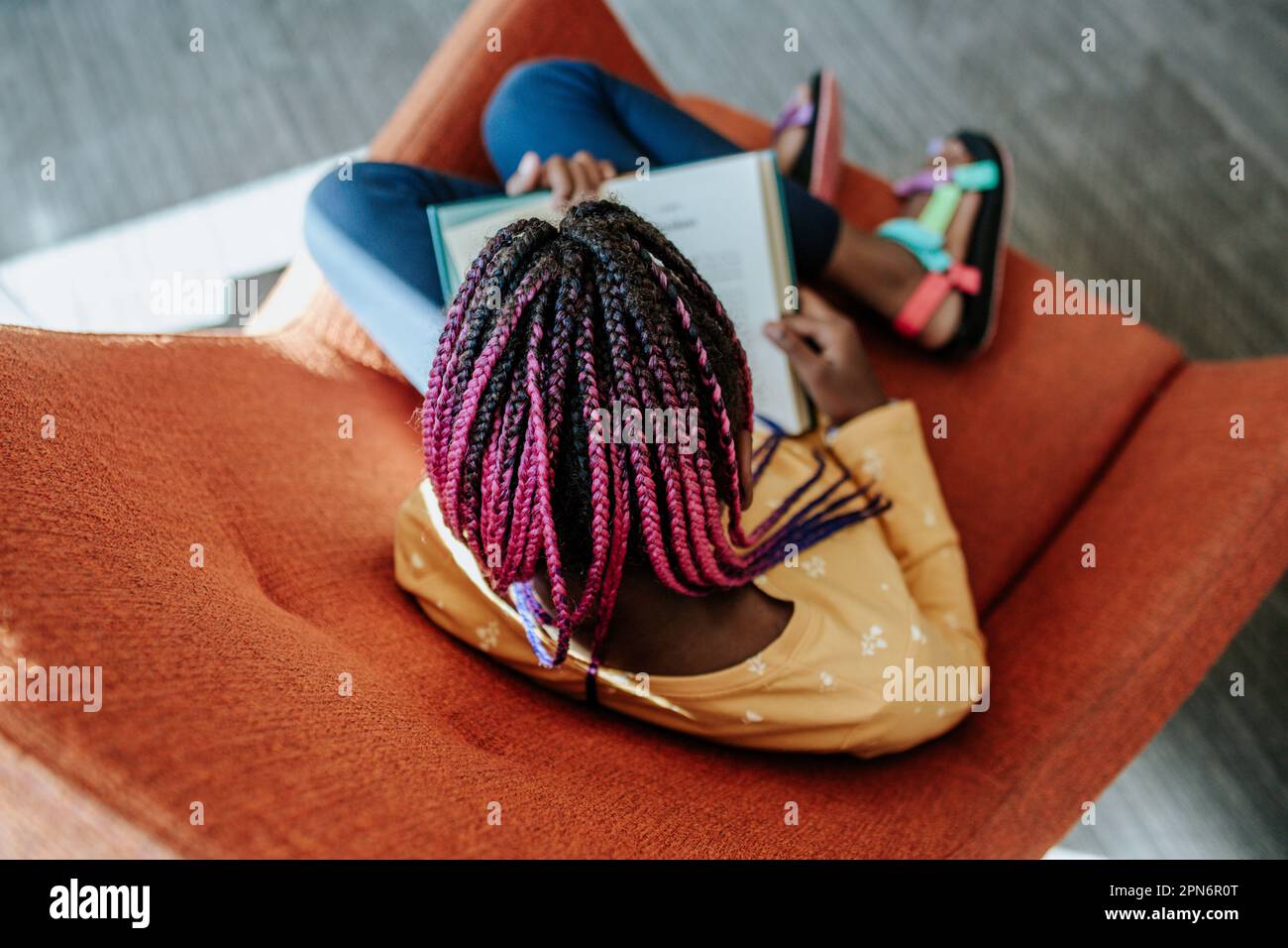 Ein junges schwarzes Mädchen, das in einem bequemen Stuhl liest Stockfoto