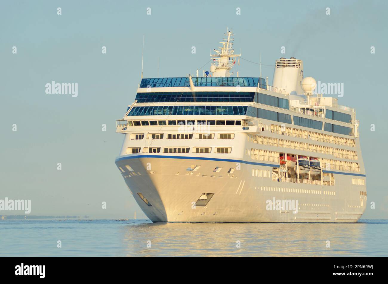 Kreuzfahrtschiff geht auf ruhiges Meer bei Sonnenaufgang und warmem Licht. Stockfoto
