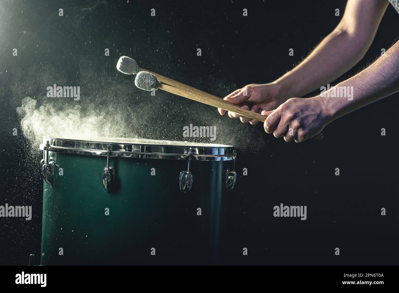 Ein Mann spielt ein musikalisches Schlaginstrument mit Stöcken auf dunklem Hintergrund. Stockfoto