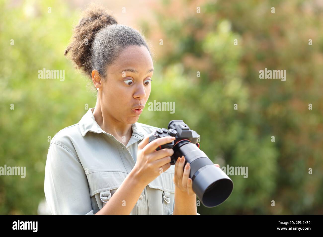 Überraschter schwarzer Fotograf, der Fotos auf einer spiegellosen Kamera in einem Park überprüft Stockfoto