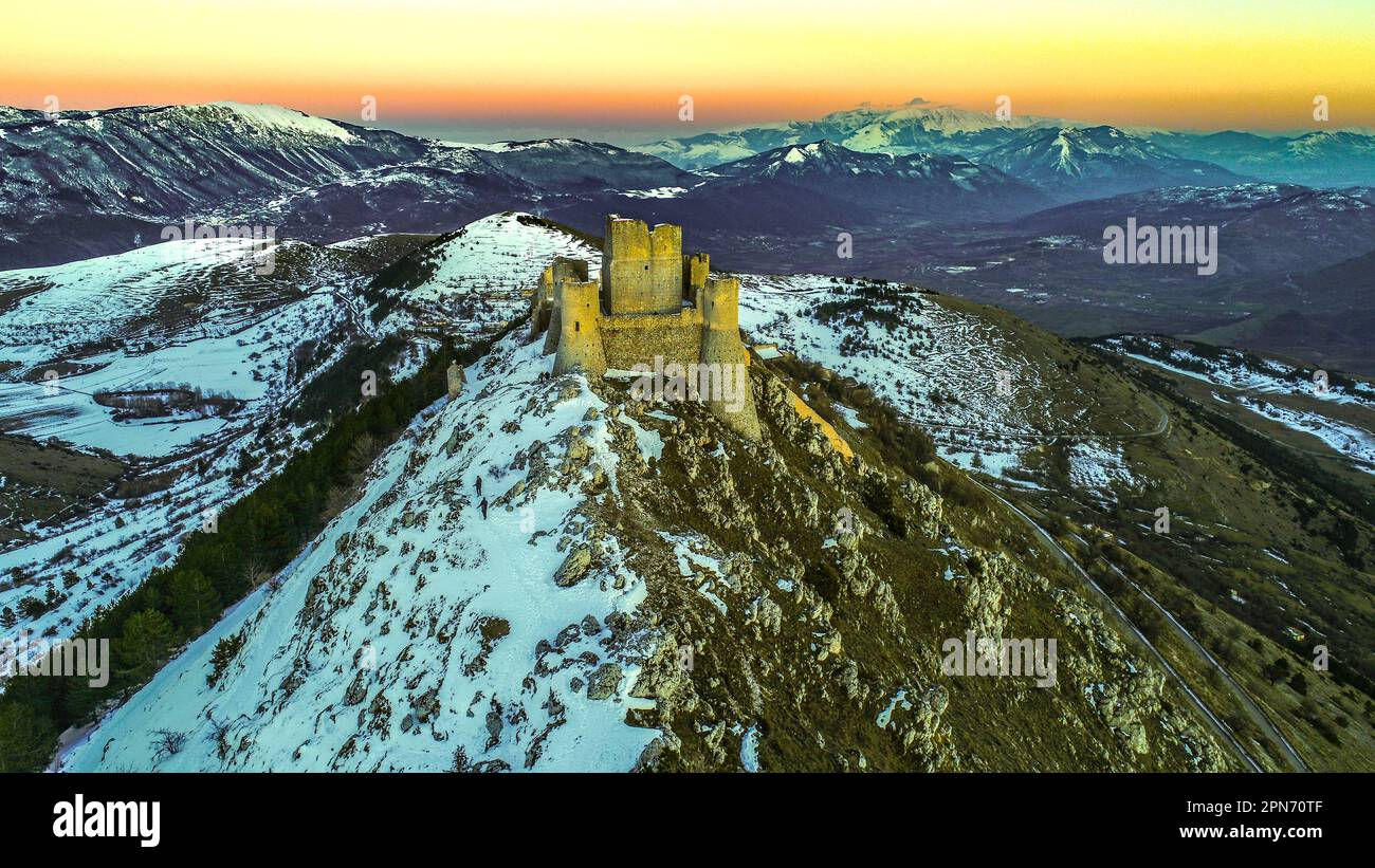 Luftaufnahme der Rocca di Calascio mit Schnee und Licht im Licht des Sonnenuntergangs, im Hintergrund die Berge des Maiella Nationalparks. Stockfoto