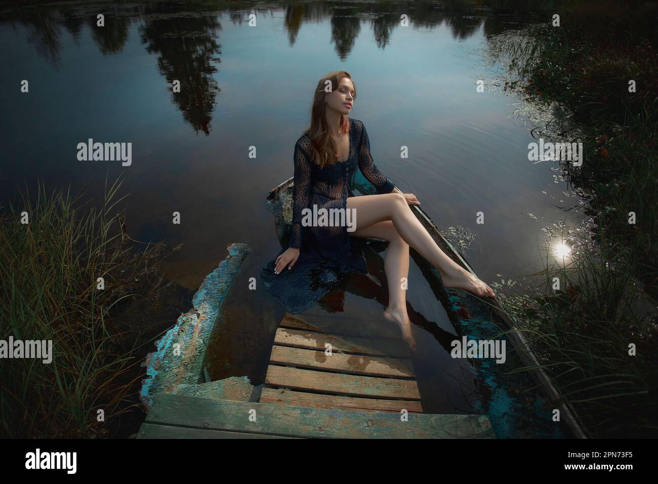 Wunderschöne romantische Frau, die in der Nähe eines Sees sitzt. Nasse Frau in Unterwäsche im Sonnenlicht bei Sonnenuntergang. Natürliche Schönheit, langes Haar Stockfoto