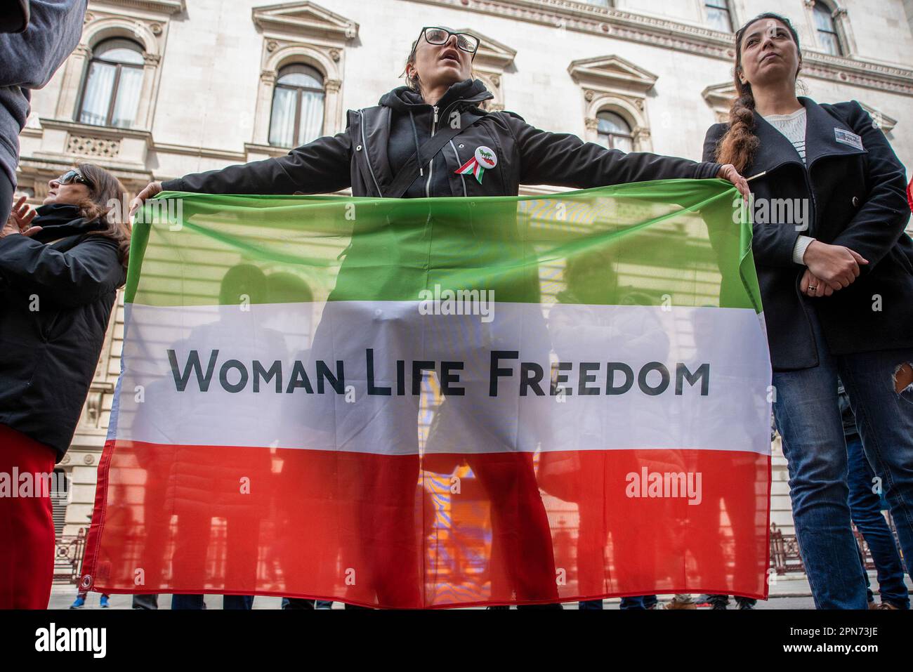 London, Großbritannien. 15. April 2023. Ein Protestteilnehmer hält während der Demonstration eine iranische Flagge, auf der "Women Life Freedom" außerhalb des Außenministeriums steht. Das iranische Volk protestiert seit dem 16. September 2022 wegen des Todes von Mahsa Amini. Die kurz nach ihrer Verhaftung wegen Verstoßes gegen das Hidschab-Gesetz des Iran starb. Laut den Augenzeugen wurde sie von der Guidance Patrol so schwer verprügelt und das verursachte ihren Tod. Kredit: SOPA Images Limited/Alamy Live News Stockfoto