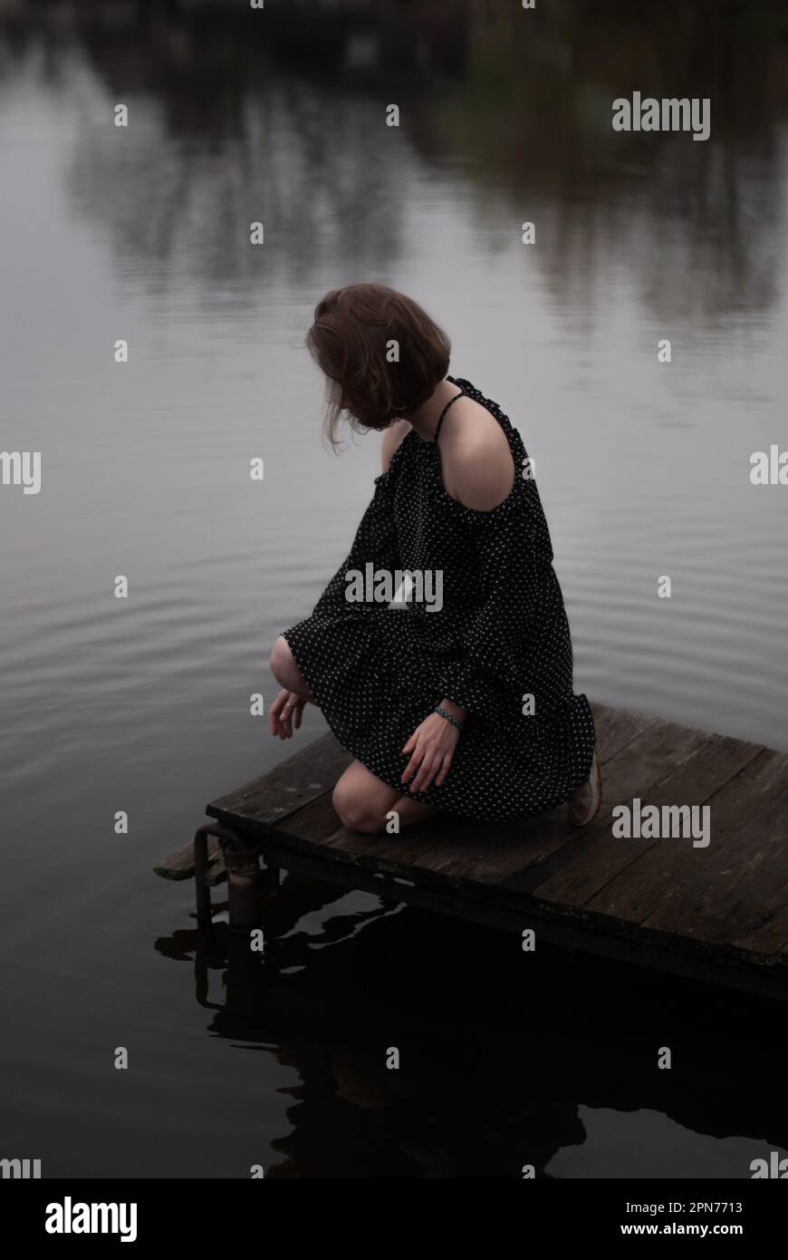 Blick auf ein Mädchen in einem Kleid in der Nähe des Sees bei bewölktem Wetter Stockfoto