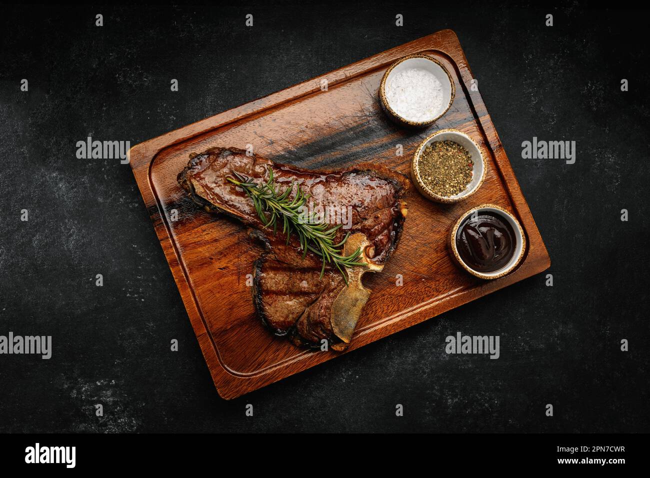 T-Bone-Steak, perfekt gegrillt mit Rosmarin und Gewürzen auf dunklem Holzbrett Stockfoto