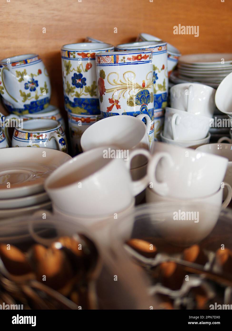 Verschiedene Tassen in einem Schrank mit Teelöffeln im Vordergrund Stockfoto