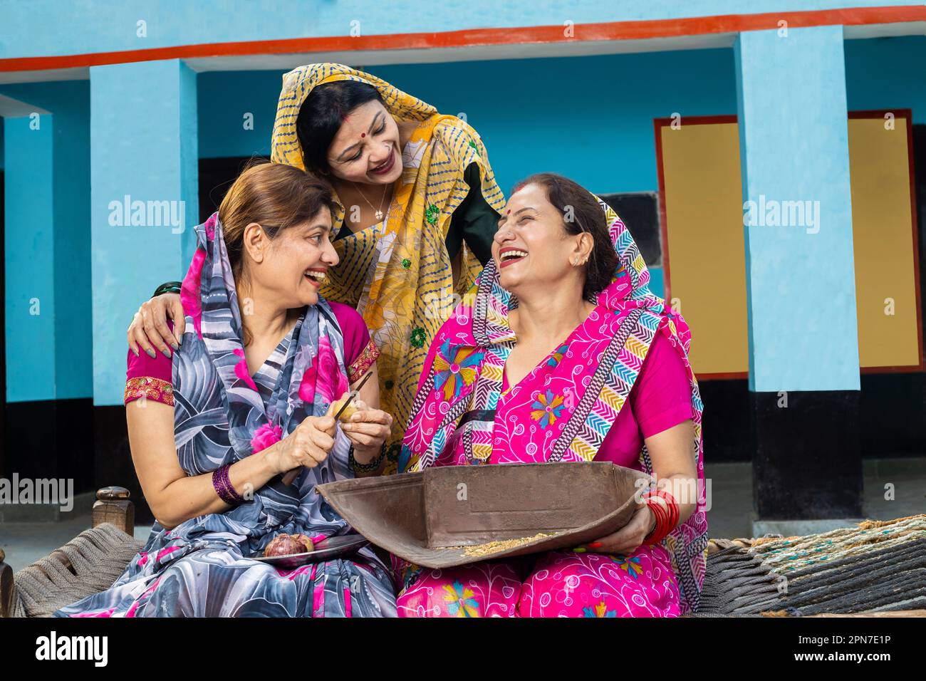 Eine Gruppe traditioneller verheirateter indischer Frauen, die Sari sprechen und lachen, arbeiten zusammen im Haushalt, um das Weinkorbsieb zu Hause zu reinigen Stockfoto