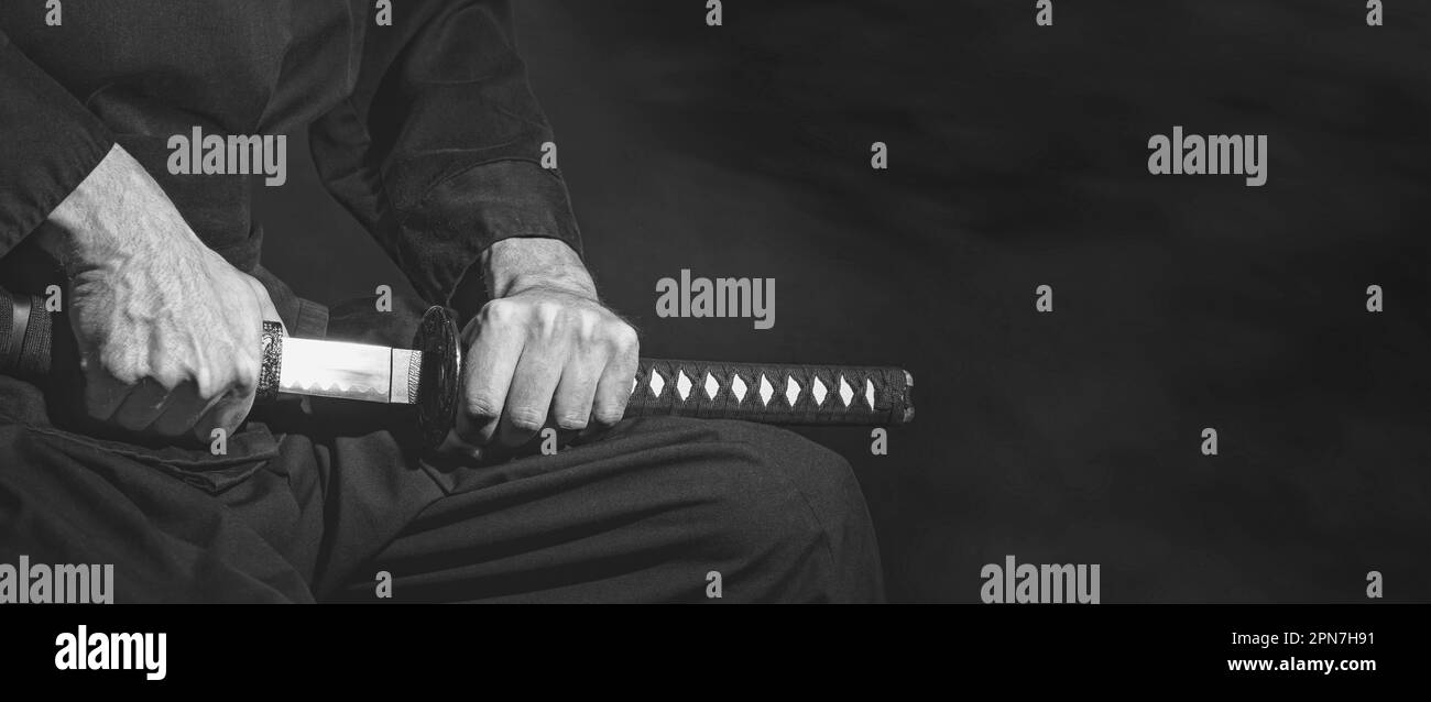 Die Samurai halten ein japanisches Katana-Schwert, ein Banner, in Schwarz und Weiß. Foto eines Kriegers in schwarzer Kleidung mit Platz für Text Stockfoto